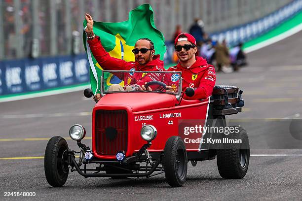 Charles Leclerc of Monaco and Ferrari shares a car with Lewis Hamilton of Great Britain and Ferrari holding a Brazil flag on the driver's parade...