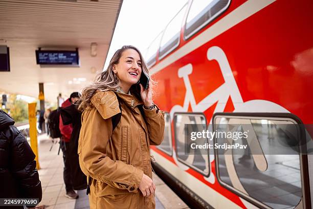 young woman in warm clothing at berlin metro station talking on a smartphone with a red train in front of her - passenger train stock pictures, royalty-free photos & images
