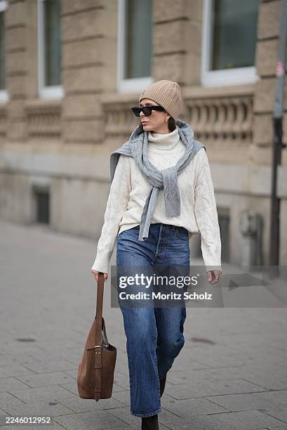 Patricia Wirschke is seen wearing a cream cable-knit turtleneck sweater by Tommy Hilfiger; a light grey cable-knit sweater draped over her shoulders...