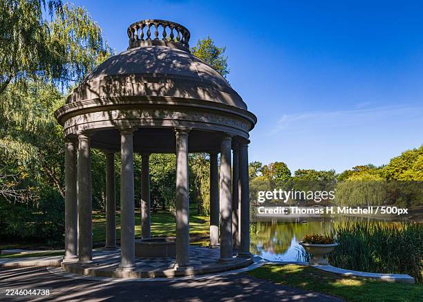 stone gazebo with a fountain in a lush park next to a tranquil pond under a clear blue sky,brookline,united states,usa,larz anderson park - brookline massachusetts stock pictures, royalty-free photos & images