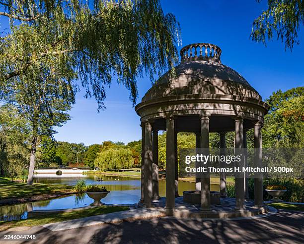 stone gazebo by a tranquil pond surrounded by lush green trees under a clear blue sky on a sunny day - brookline massachusetts stock pictures, royalty-free photos & images