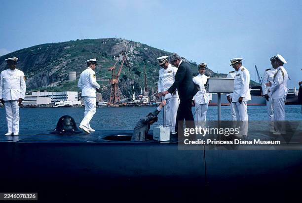 As Brazilian naval officers & other dignitaries stand by, Prince Charles, Prince of Wales climbs out of the hatch of the Brazilian submarine...