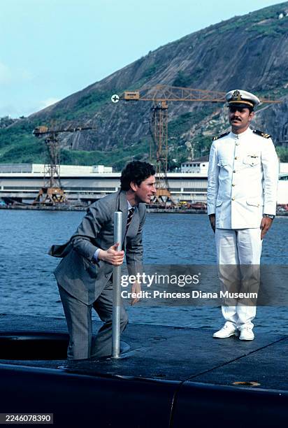 As an unidentified Brazilian naval officer stands by, Prince Charles, Prince of Wales climbs out of the hatch of the Brazilian submarine Riachuelo ,...