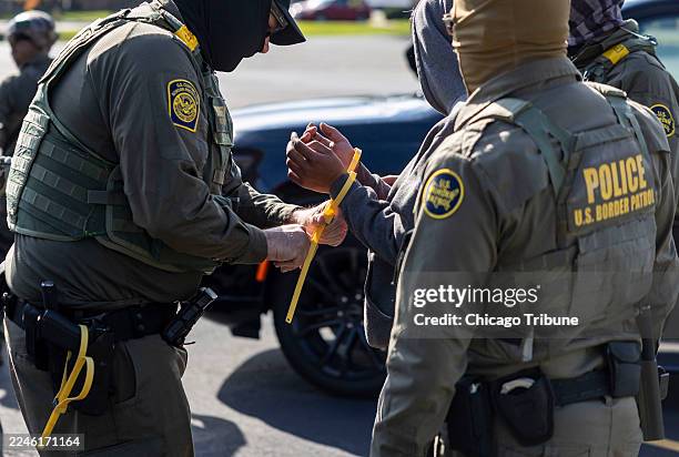 Border Patrol agents exchange handcuffs for plastic zipties while transferring detainees they picked up landscaping on Chicago's Northwest Side into...