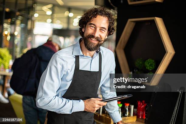 kellner lächelt, während er eine speisekarte in einem restaurant hält - die neue normalität stock-fotos und bilder