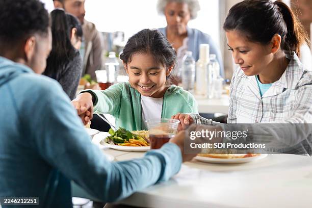 multi-generational family holds hands in prayer before sharing a meal together. - food security stock pictures, royalty-free photos & images