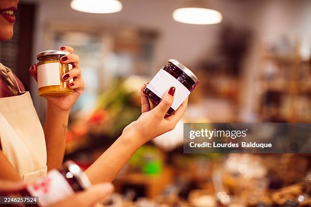 woman holding glass jars of organic jam at local store - jam jar stock pictures, royalty-free photos & images