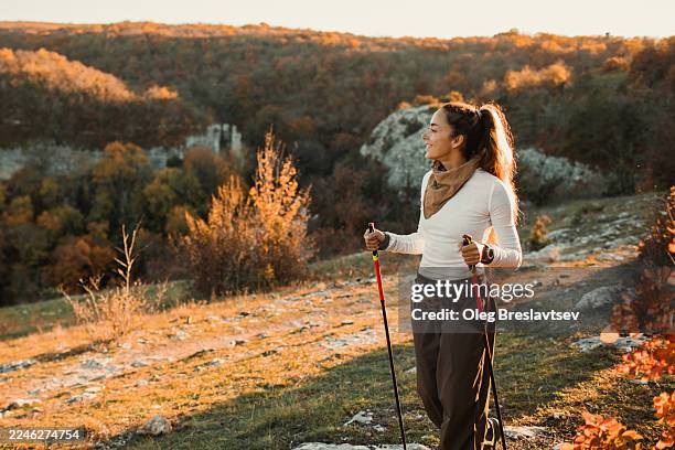 woman nordic walking on autumn hillside at sunset with hiking poles. scenic landscape on background - ropa de deporte fotografías e imágenes de stock