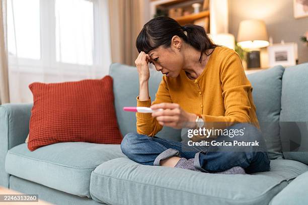asian woman feeling worried seeing positive pregnancy test result - infertility stock pictures, royalty-free photos & images