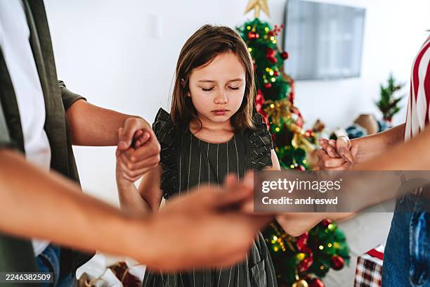 little girl praying with family holding hands during christmas at home - family worship stock pictures, royalty-free photos & images
