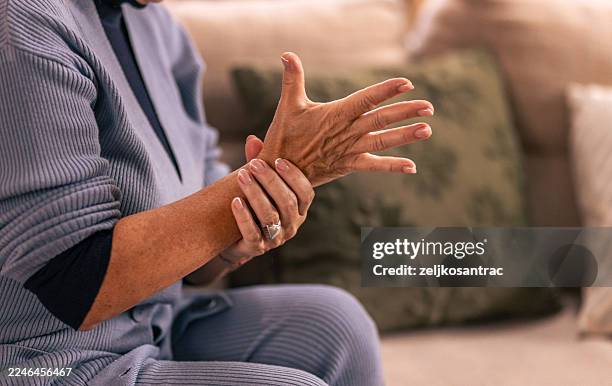 senior woman experiencing hand pain tingling at home - chronic illness stock pictures, royalty-free photos & images