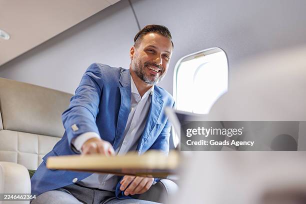 smiling businessman working and traveling in a private jet cabin - first class stock pictures, royalty-free photos & images