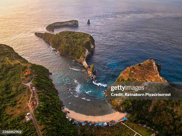 stunning aerial views of diamond and atuh beach in nusa penida, indonesia. rugged cliffs, turquoise ocean, rock arches, and tropical coastline illuminated by golden sunrise and dramatic light - nusa penida stock pictures, royalty-free photos & images