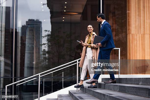professional business partners descend stairs outside modern building in nyc, carrying folders and tablet - business meeting stockfoto's en -beelden
