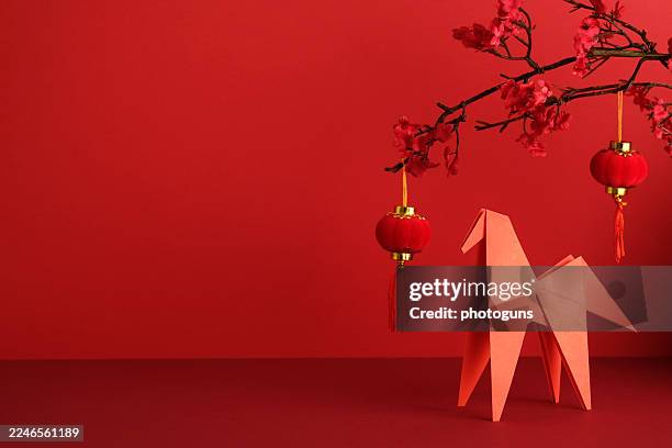 Chinese New Year setup with an origami paper horse, red lantern, and plum blossom branch against a bright red background. Ideal for Year of the Horse and Asian greeting card design