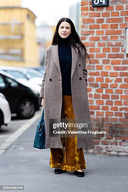 Passerby wears a brown, checked long coat over a navy turtleneck sweater and ochre velvet wide-leg trousers, accessorized with black ballet flats and...