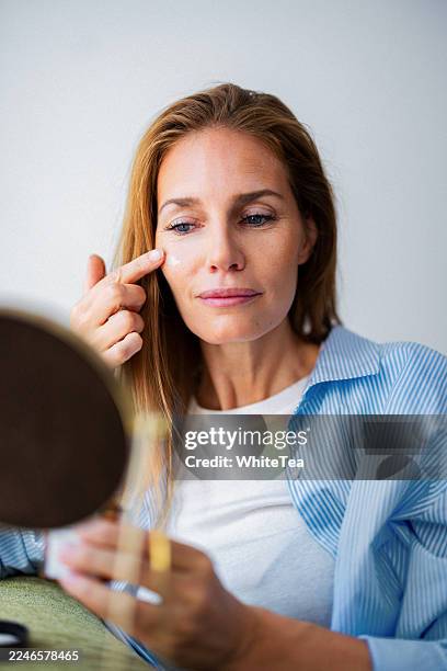 woman applies under-eye cream in mirror view during casual home skincare routine - facial oil stock pictures, royalty-free photos & images
