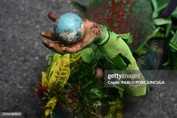 An Indigenous man performs lying on the ground while holding a globe in his hand during the "Indigenous People Global March" at the COP30 UN Climate...