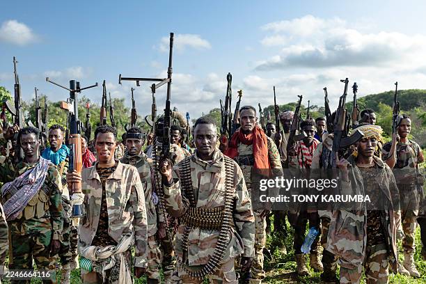 Soldiers of the Somalia National Army raise their weapons when they gathered near their camp for a talk from visiting senior officers at Awdheegle,...