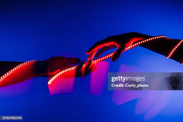 two human hands interact with a glowing, wavy line of red light, creating an abstract, dynamic connection against a deep blue background. - linking hands stock pictures, royalty-free photos & images
