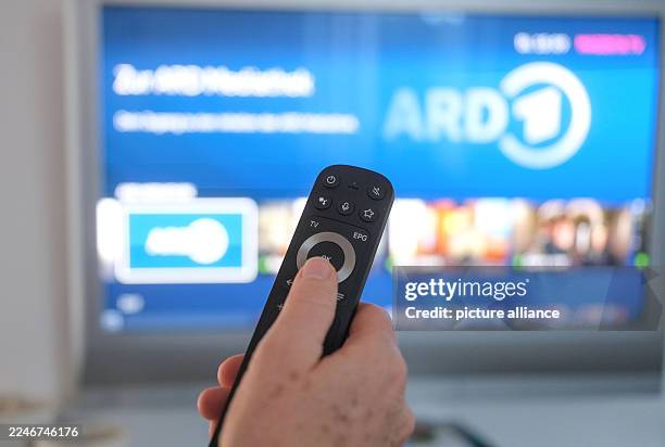 November 2025, Baden-Württemberg, Stuttgart: One hand holds a remote control and points to a switched-on television, on whose screen the user...