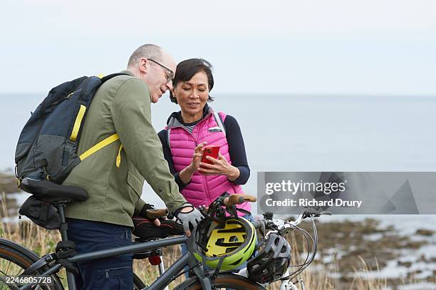 senior cyclist couple using a smart phone for directions - real couple stock pictures, royalty-free photos & images