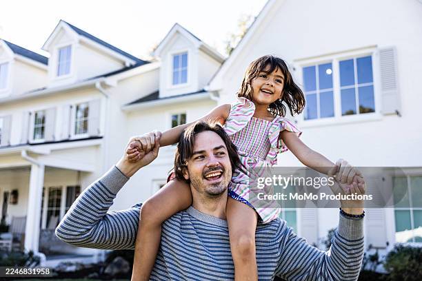young girl riding on her fathers shoulders in front of suburban home - carrying on shoulders stock pictures, royalty-free photos & images
