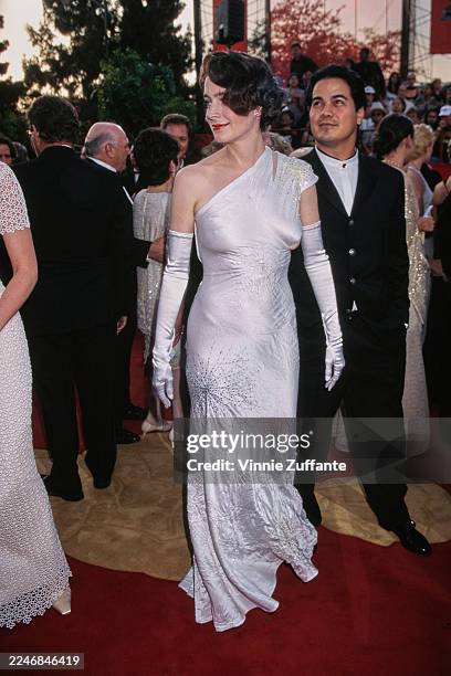 American actress Sean Young, wearing a white one-shoulder evening gown with white evening gloves, and her husband, American actor Robert Lujan, who...