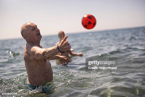 multi generation family playing with ball on the beach, senior man tries to reach the ball - grandpa playing catch stock pictures, royalty-free photos & images