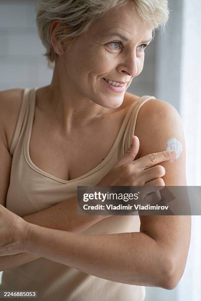 eine reife frau trägt östrogen auf ihren arm auf - östrogen stock-fotos und bilder