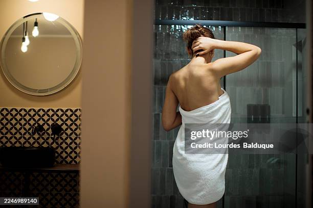 woman wrapped in towel standing in modern bathroom - envuelto en una toalla fotografías e imágenes de stock