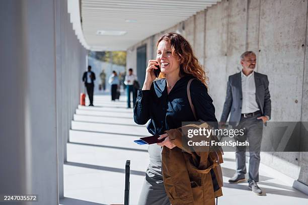 donna d'affari che cammina in un corridoio moderno mentre è al telefono, portando cappotto e documenti - viaggio di lavoro foto e immagini stock