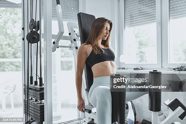 fit woman using leg curl machine in modern gym during intense training session - leg curl gym stock pictures, royalty-free photos & images