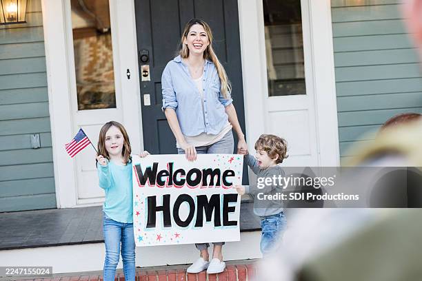 family excitedly welcomes someone home with a 'welcome home' sign and an american flag. - welcome home stock pictures, royalty-free photos & images