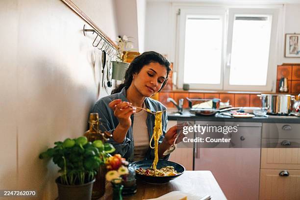 woman enjoying spaghetti at home kitchen table - day in the life series stock pictures, royalty-free photos & images