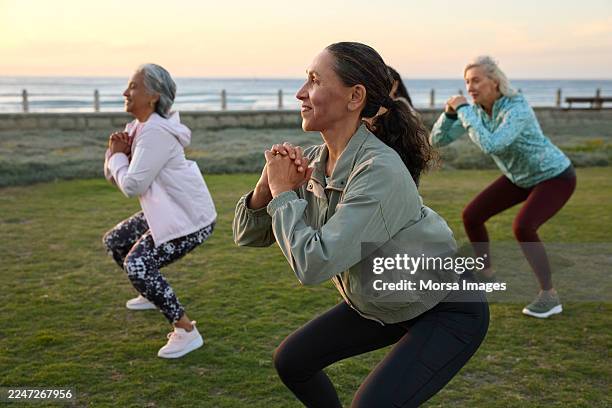 smiling woman squatting while doing exercise with friends - hockend stock-fotos und bilder