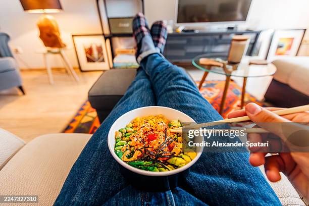 man eating poke bowl using chopsticks at home, personal perspective view - couch potato refrán en inglés fotografías e imágenes de stock