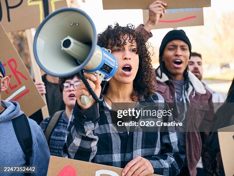 Diverse group of people holding signs as a woman speaks through a megaphone at a positive community rally Diverse group of people holding signs as a woman speaks through a megaphone at a positive community rally