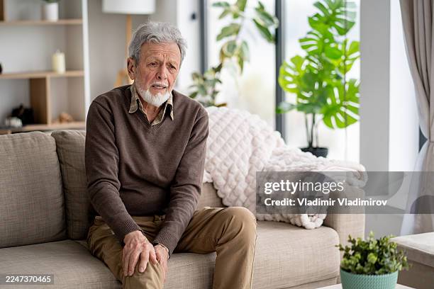 elderly man with thoughtful expression sitting on couch - blodpropp bildbanksfoton och bilder