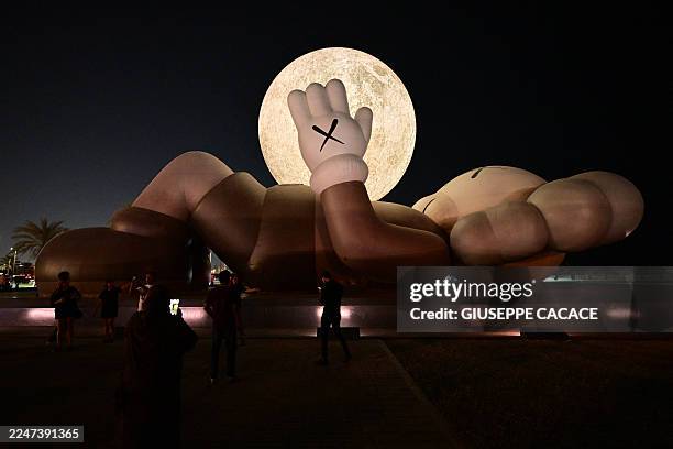 Visitors look at the "KAWS:HOLIDAY" art installation featuring the "COMPANION" figure created by US artist Brian Donnelly, also known as Kaws, during...