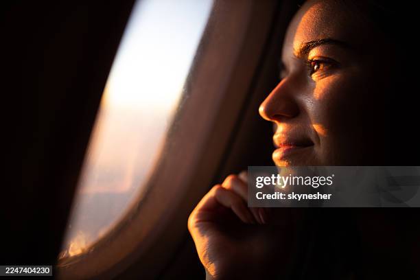 primo piano di una donna sorridente che guarda il tramonto attraverso il finestrino dell'aereo. - guardare fuori dalla finestra foto e immagini stock