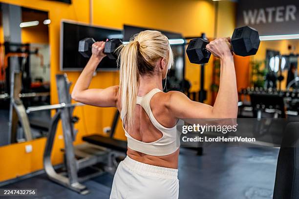 frau, die im fitnessstudio kurzhanteln hebt - schulterpresse stock-fotos und bilder