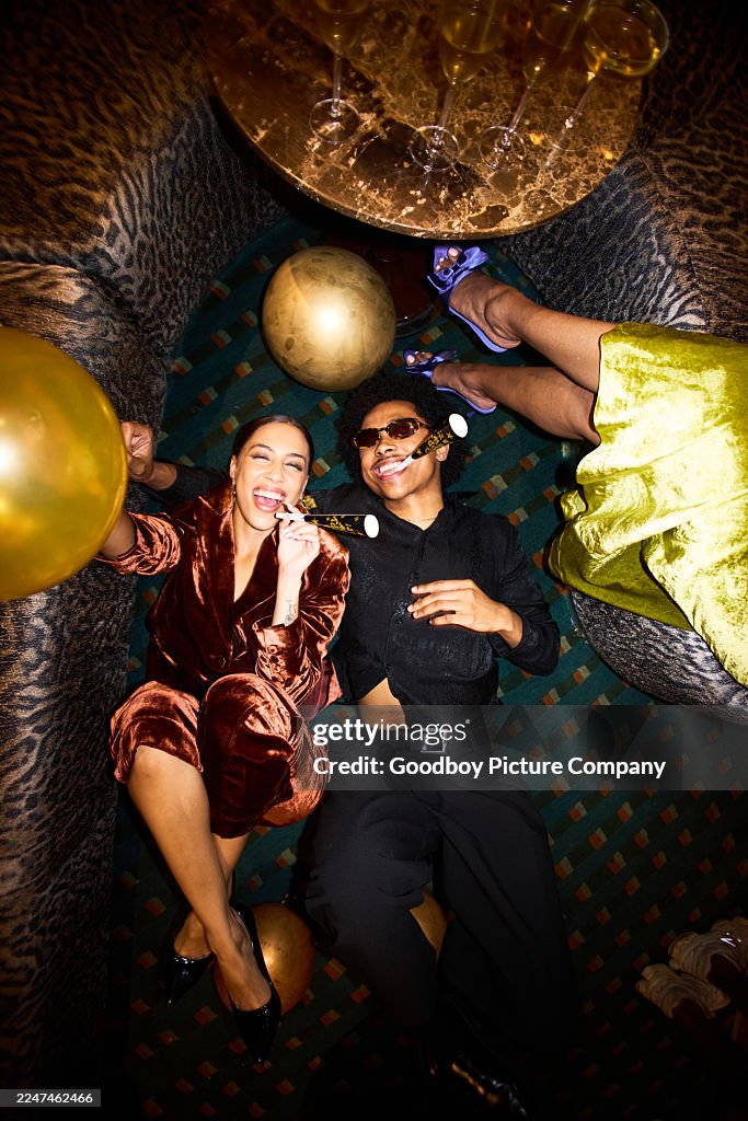 Top view of joyful friends lying on patterned floor surrounded by gold balloons at a fun New Year’s Eve celebration