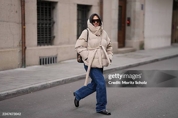 Anna Winter is seen wearing an oversized beige Steilia brushed down puffer jacket with a high padded collar, hood and belted waist from Holzweiler; a...