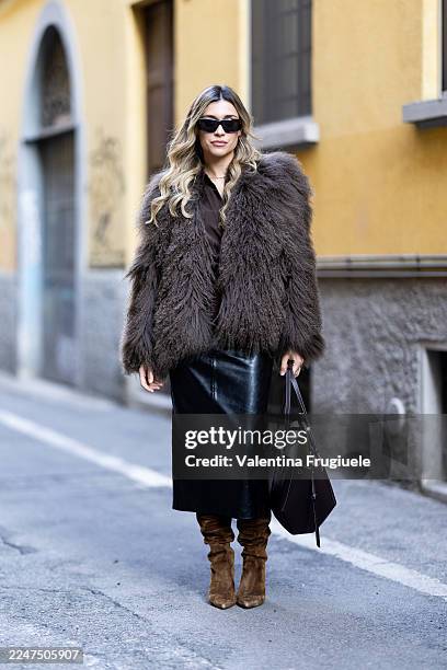 Guest wears a voluminous brown shearling jacket, black leather midi skirt, slouchy brown suede heeled boots and black sunglasses, carrying a...