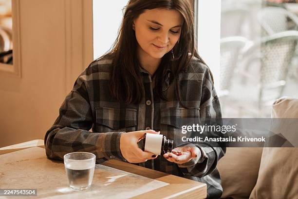 young woman in plaid shirt at cafe applying lotion from bottle, a calm skincare moment - biodegradável imagens e fotografias de stock