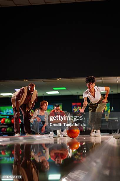 junge frau wirft eine bowlingkugel, während freunde sie anfeuern, und genießt gemeinsam ein lebhaftes spiel in der bowlingbahn - bowlingbahn stock-fotos und bilder