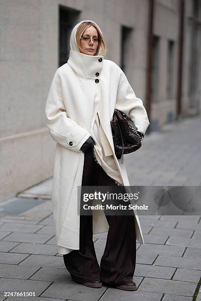 Anouk Delphine is seen wearing a long cream wool coat with a high stand collar, dropped shoulders and large contrast buttons from Mango; layered...