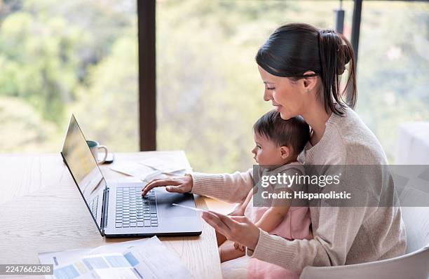 loving mother paying bills at home while caring for her baby daughter - life balance stock pictures, royalty-free photos & images