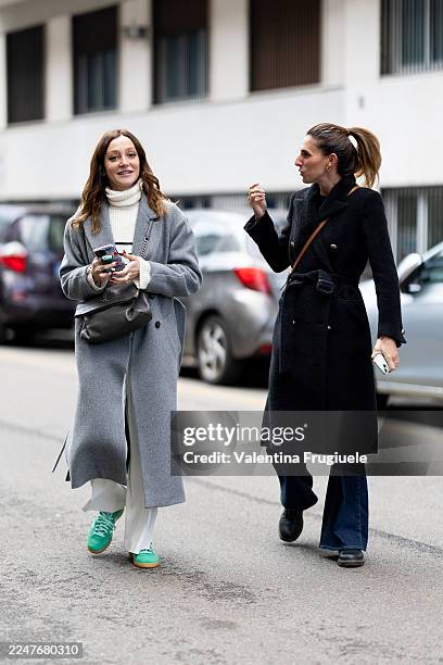 Passerby wears a long grey wool coat layered over a chunky white turtleneck sweater, wide white trousers and bright green low-top sneakers,...